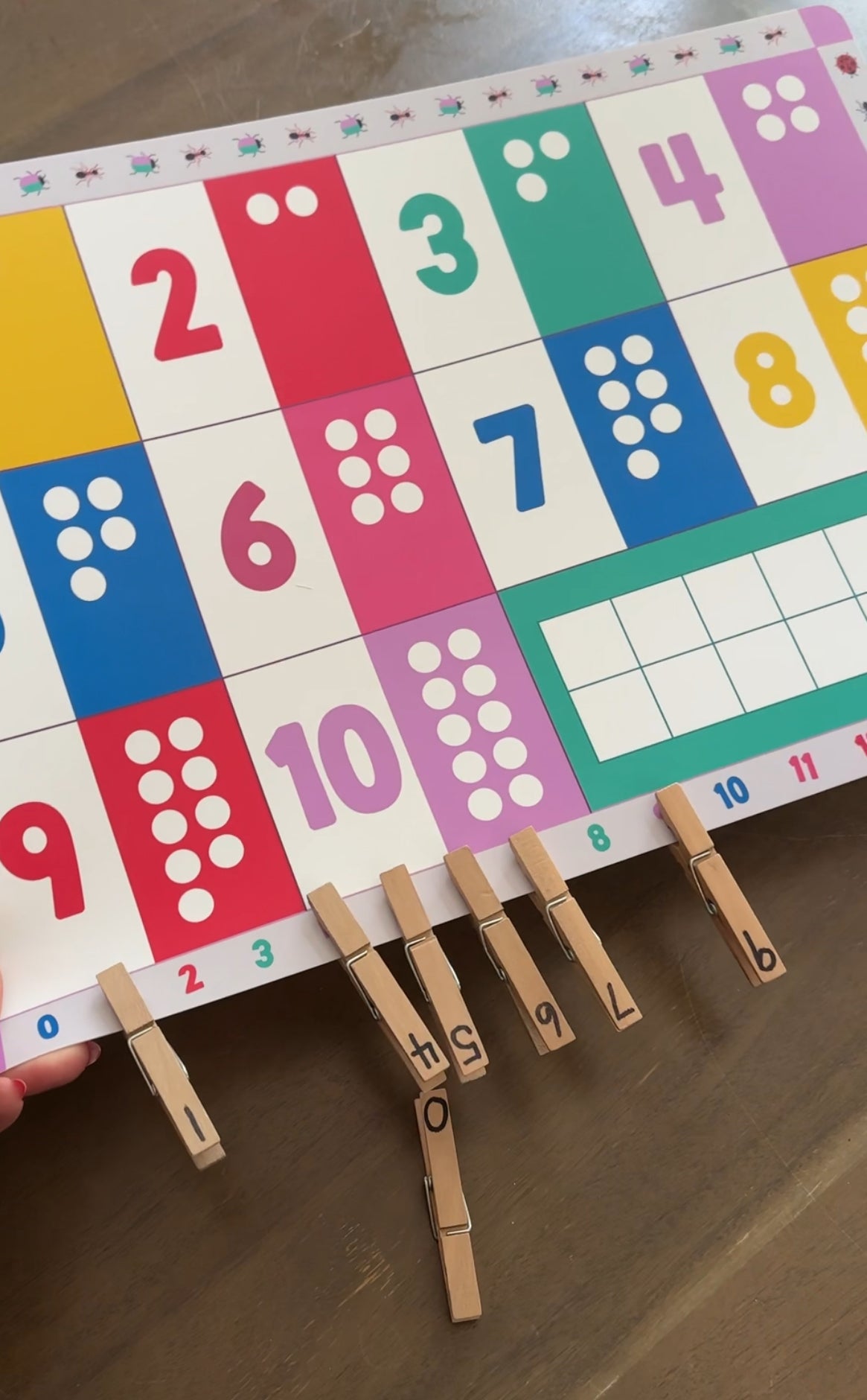 Child pinching numbered clothespins and matching them to the correct numbers on the number line printed along the edge of the Domino & Juliette Numbers Placemat.